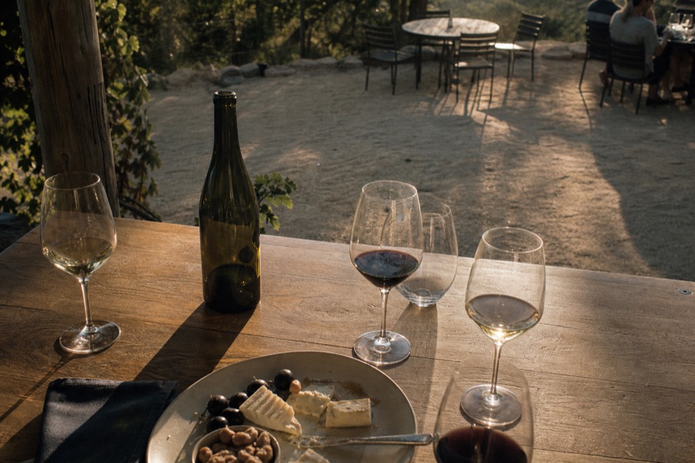 An overhead view of a tasting table with several wine glasses, a cheese plate, a bottle and a folded napkin in warm natural light, no text, no logos, no people