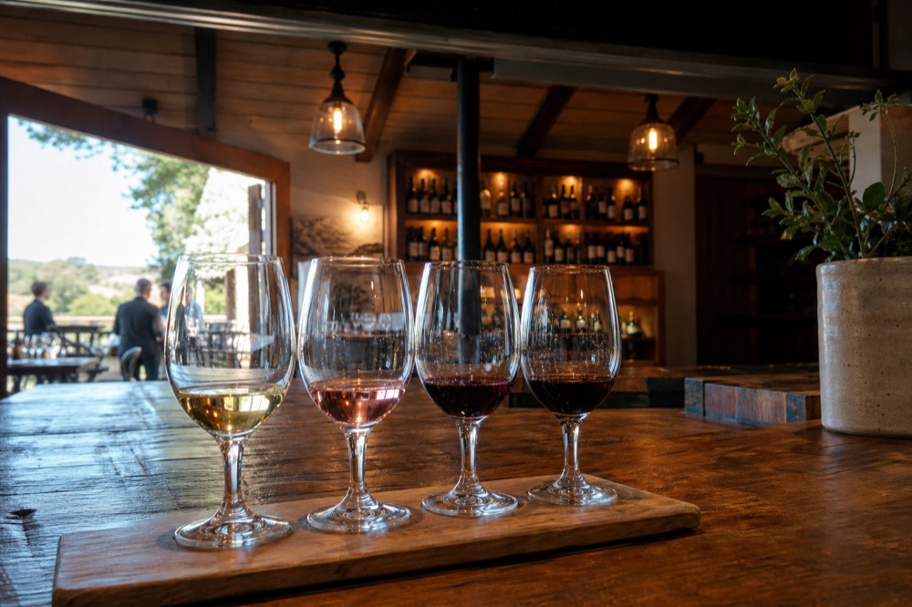 A tasting flight of wine glasses on a rustic wooden counter inside a warm-lit village tasting room, no text, no logos, no people