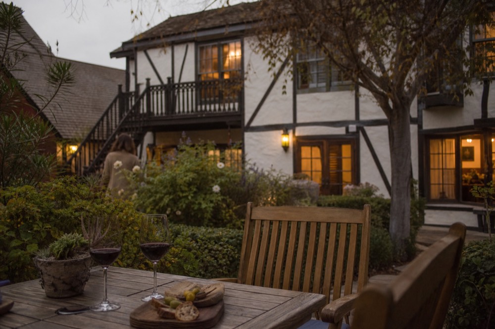A cozy Solvang inn courtyard at dusk with warm window light and a small table set with wine glasses, half-timbered walls behind, no text, no logos, no people