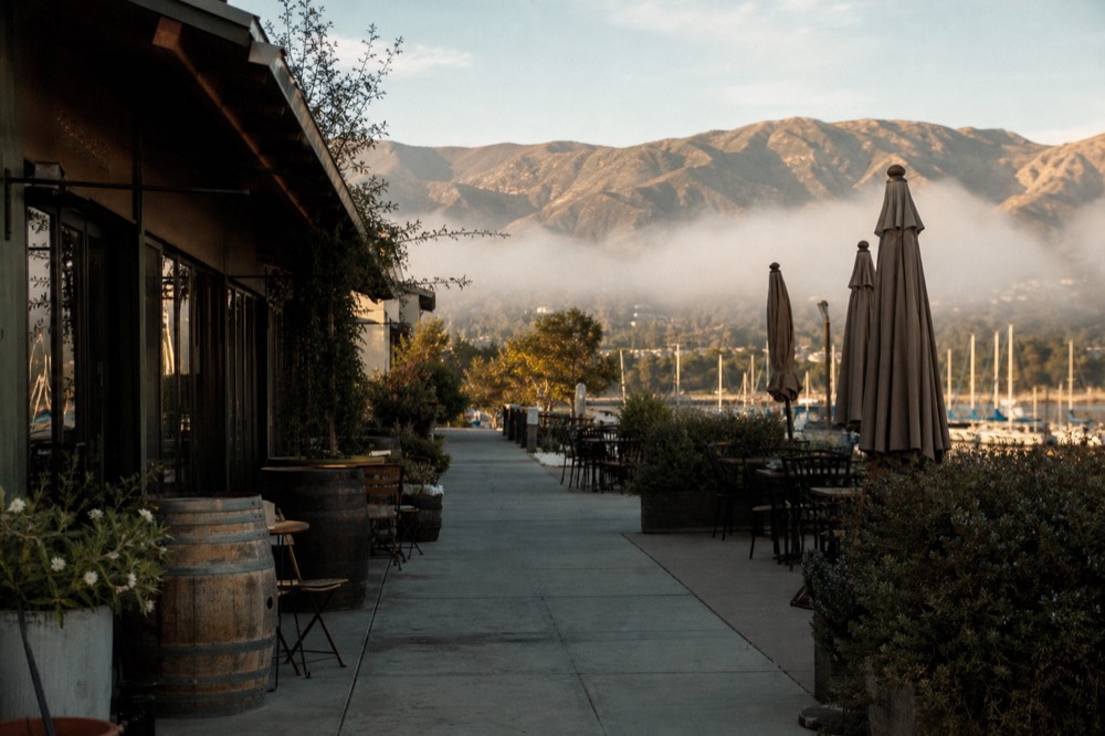 A walkable district of low tasting-room storefronts and sidewalk tables a short distance from a harbor, no text, no logos, no people