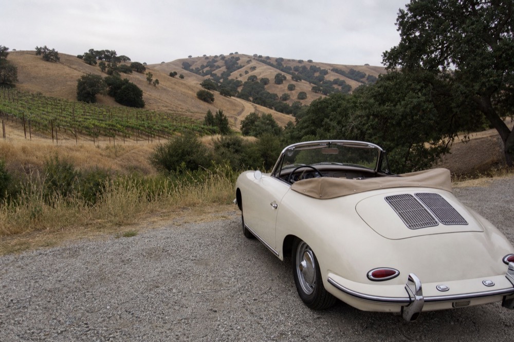 A vintage convertible parked on a gravel shoulder beside golden oak-studded vineyard hills in the inland Santa Ynez Valley, no text, no logos, no people