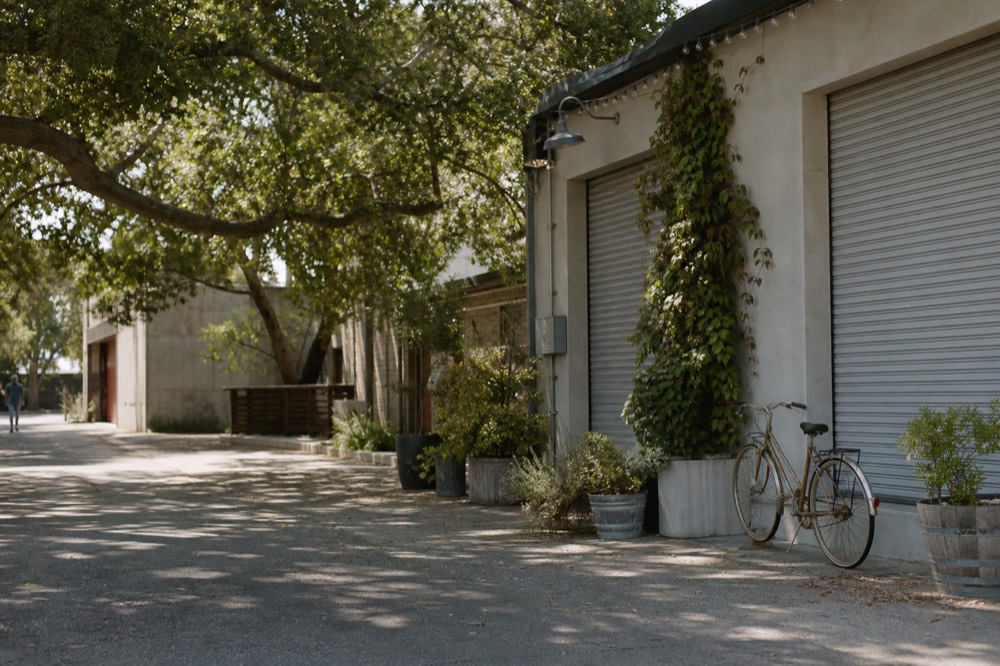 A quiet morning view of Funk Zone tasting-room storefronts with chalkboard-free facades, roll-up doors still closed and a bicycle parked outside, no text, no logos, no people
