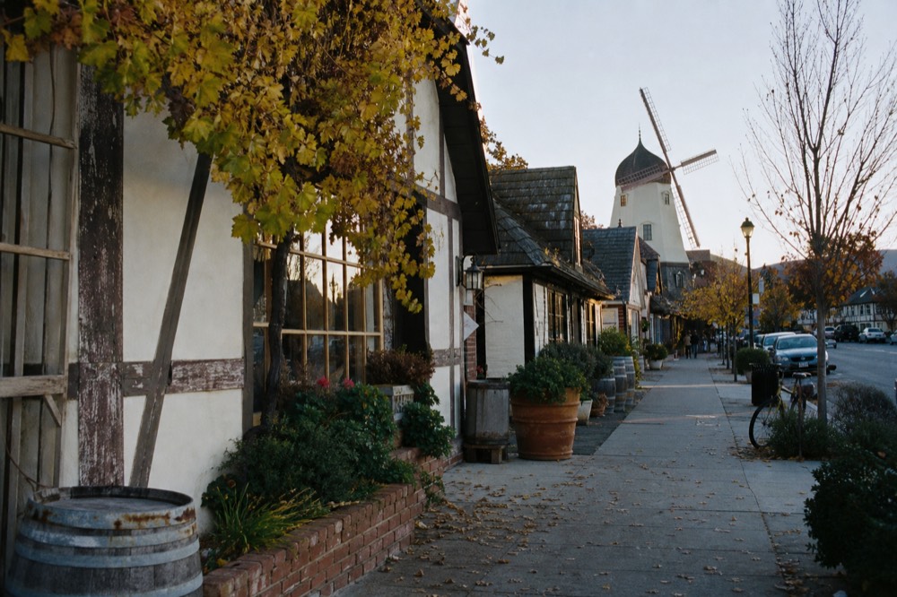 A quiet Solvang street at golden hour with half-timbered buildings and a wooden windmill, potted flowers along the sidewalk, no text, no logos, no people